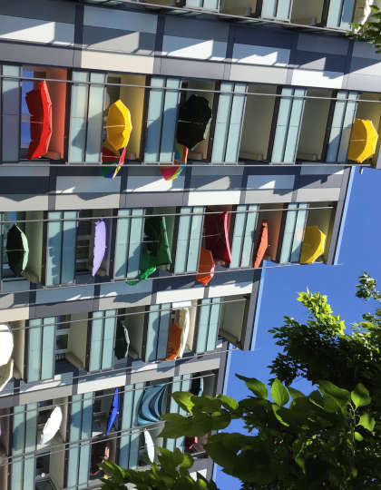 Außenansicht des Wohnstifts. Auf den Balkonen sind viele bunte Sonnenschirme zu sehen.