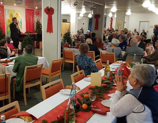 Das Bild zeigt die Weihnachtsfeier 2024. Zu sehen sind zahlreiche geschmückte und gut besetzte Tische sowie ein Redner.